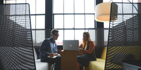 Zwei Menschen vor einem Laptop an einem Tisch